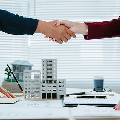 Une poignée de main avec en arrière-plan une maquette d'un immeuble d'habitation