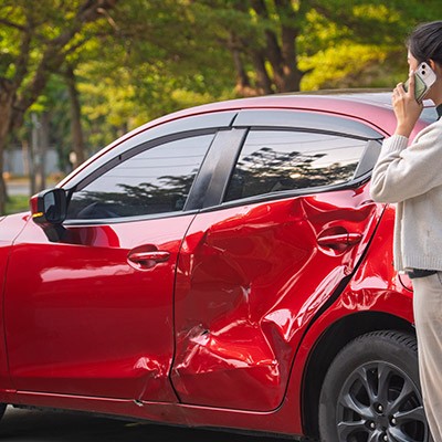 Une femme au téléphone devant sa voiture rouge accidentée