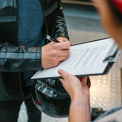 Un homme, casque à la main, signant une assurance pour sa moto