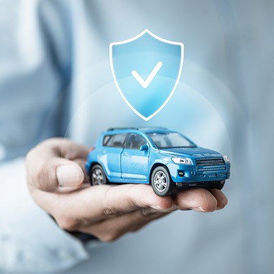 Un homme tenant une voiture miniature avec un bouclier représentant l'assurance