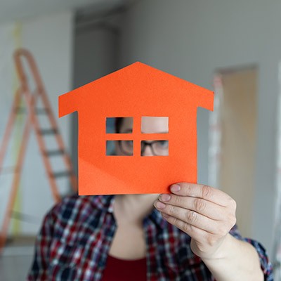 Une femme dans une maison en rénovation tenant fièrement une maison en papier orange